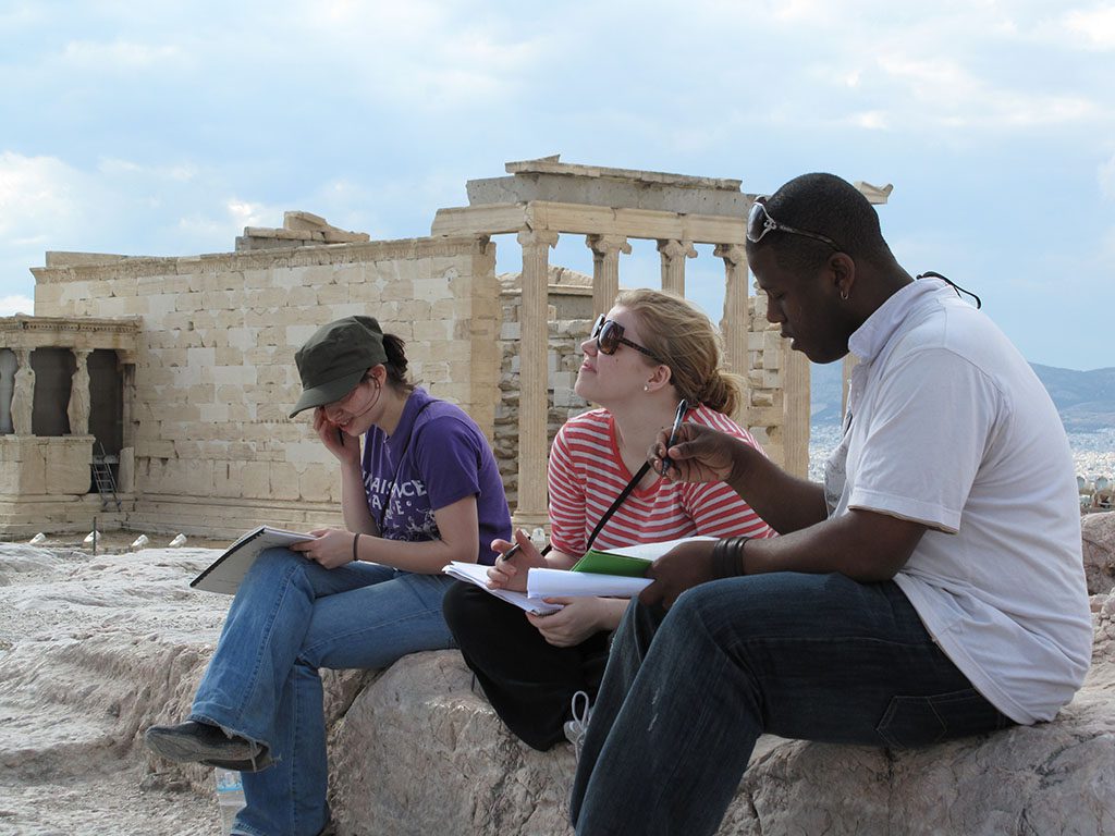 Students near monument in Greece working on assignments