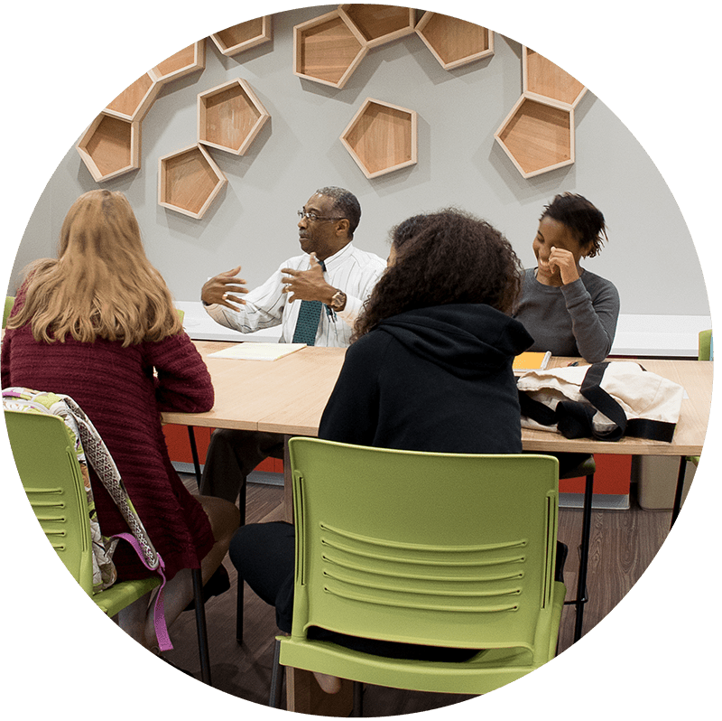 Students and professor sitting around table, engaging in conversation