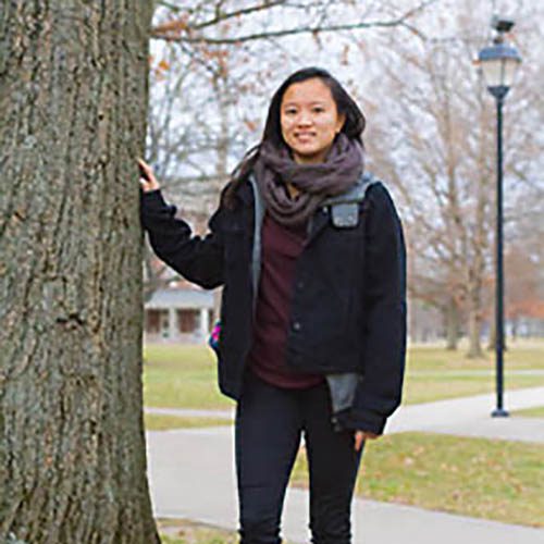 Mia Kaplan, Earlham class of 2018, stands next to a tree on campus