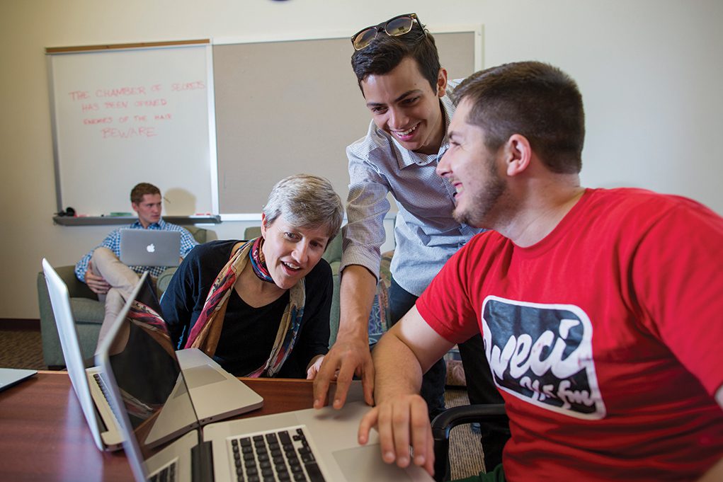 Professor and two students collaborating while using their laptops