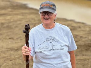 Patricia Thomas holds a walking stick wearing a hat with the words Pastor and Professor Mystery Series