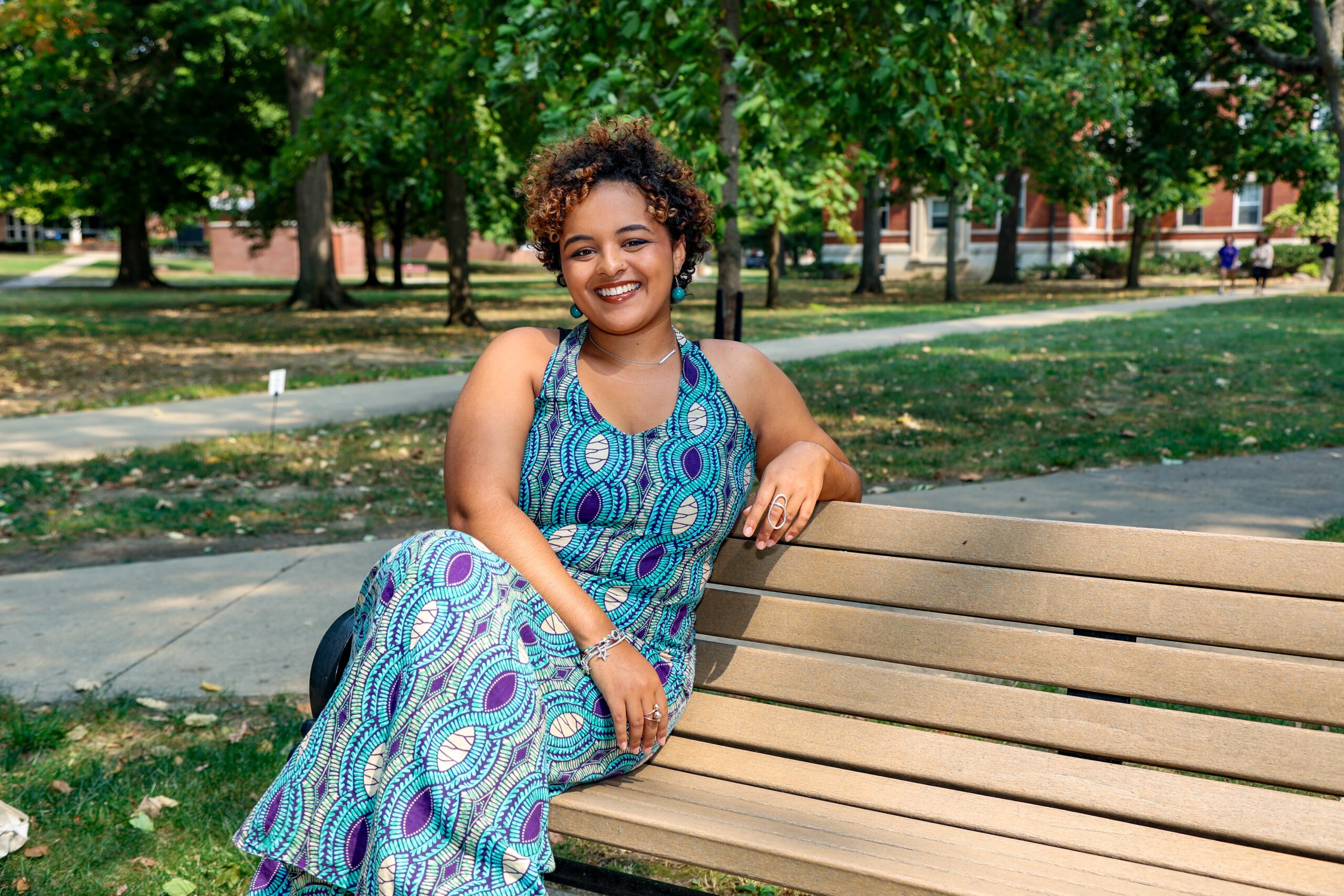 Earlham College student Maellyn Kururanga sits at a bench wearing a blue dress with her legs crossed