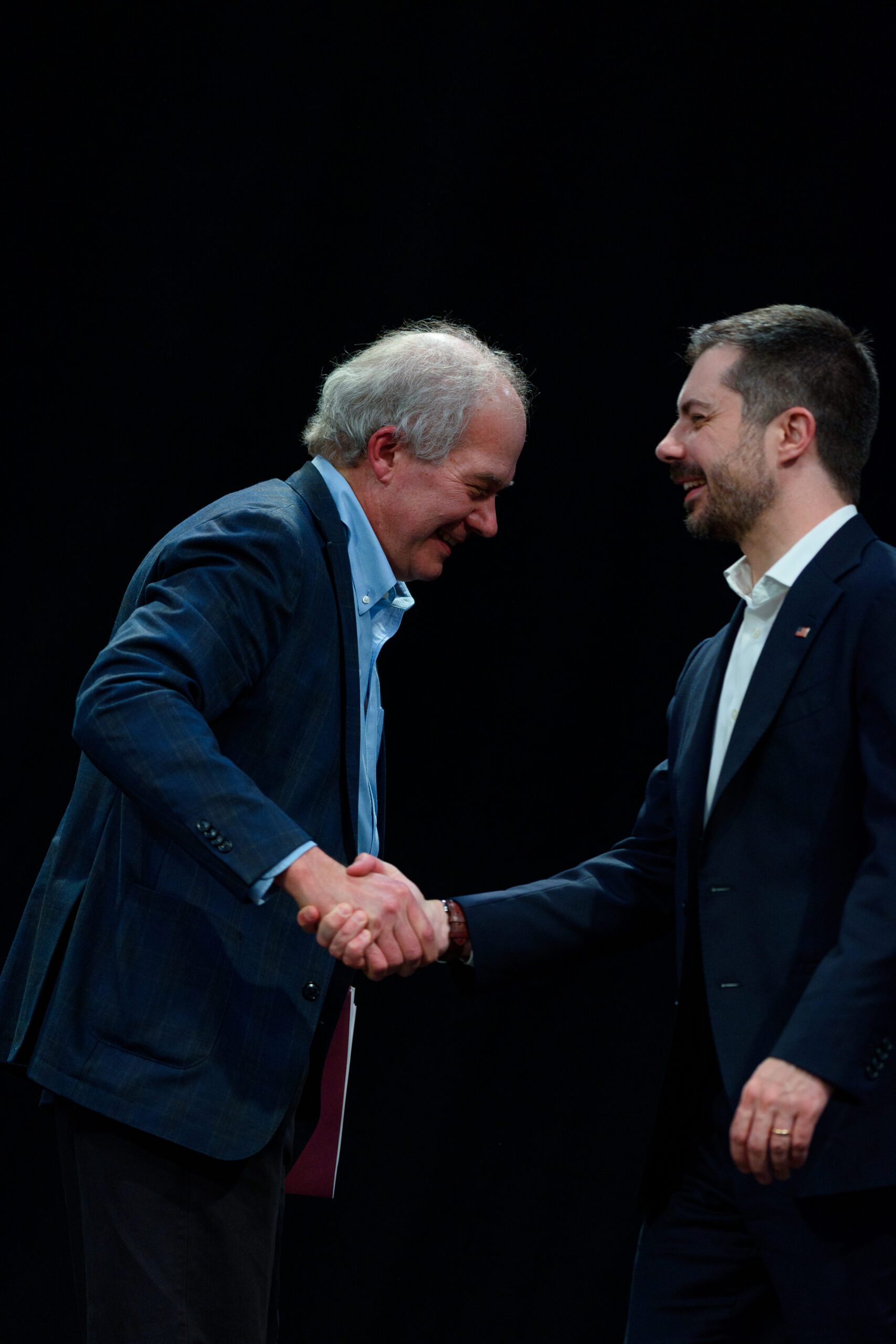 Pete Buttigieg appears at the right with his arm extended to shake the hand of Paul Sniegowski