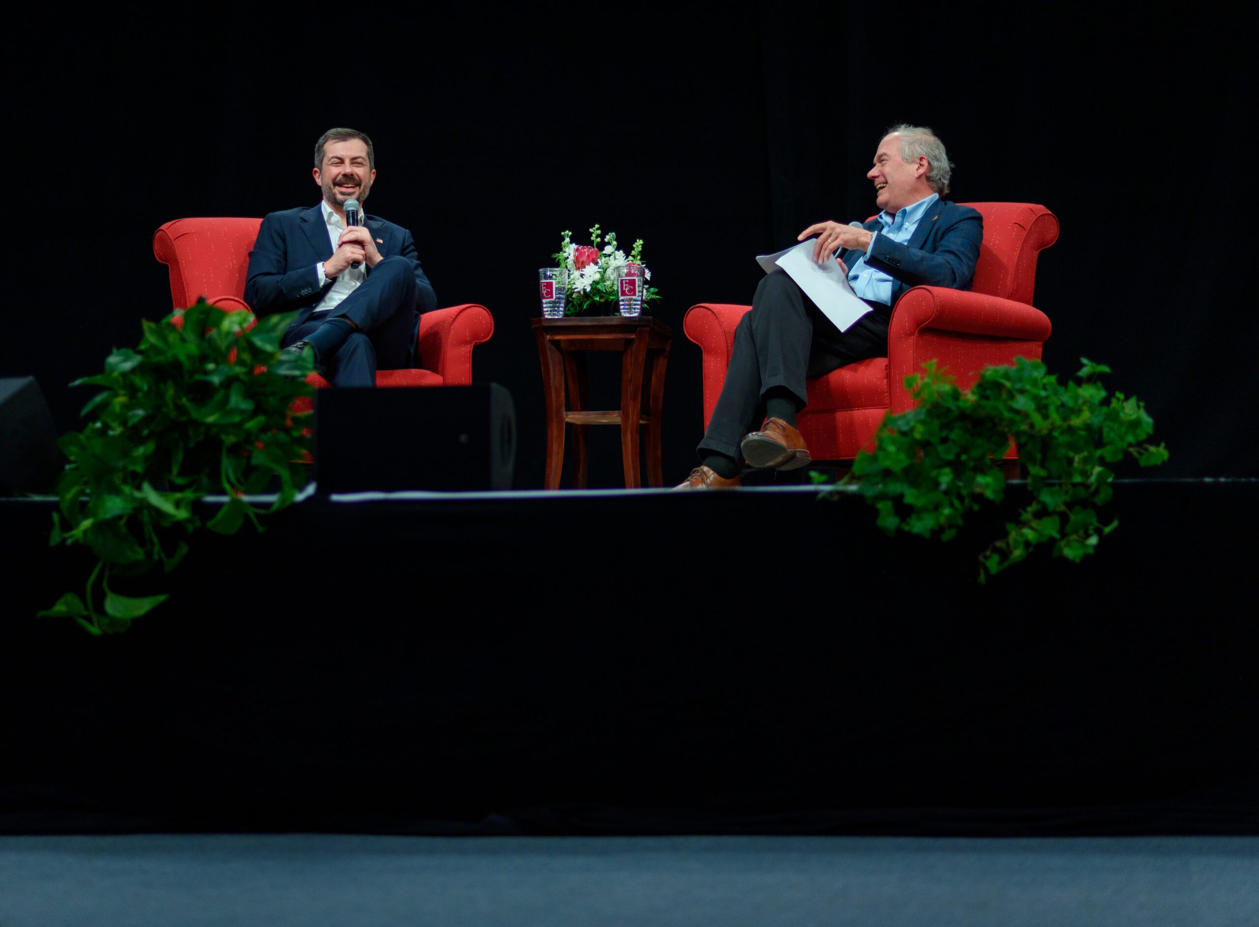 Pete Buttigieg and Paul Sniegowski seated in red chairs laughing