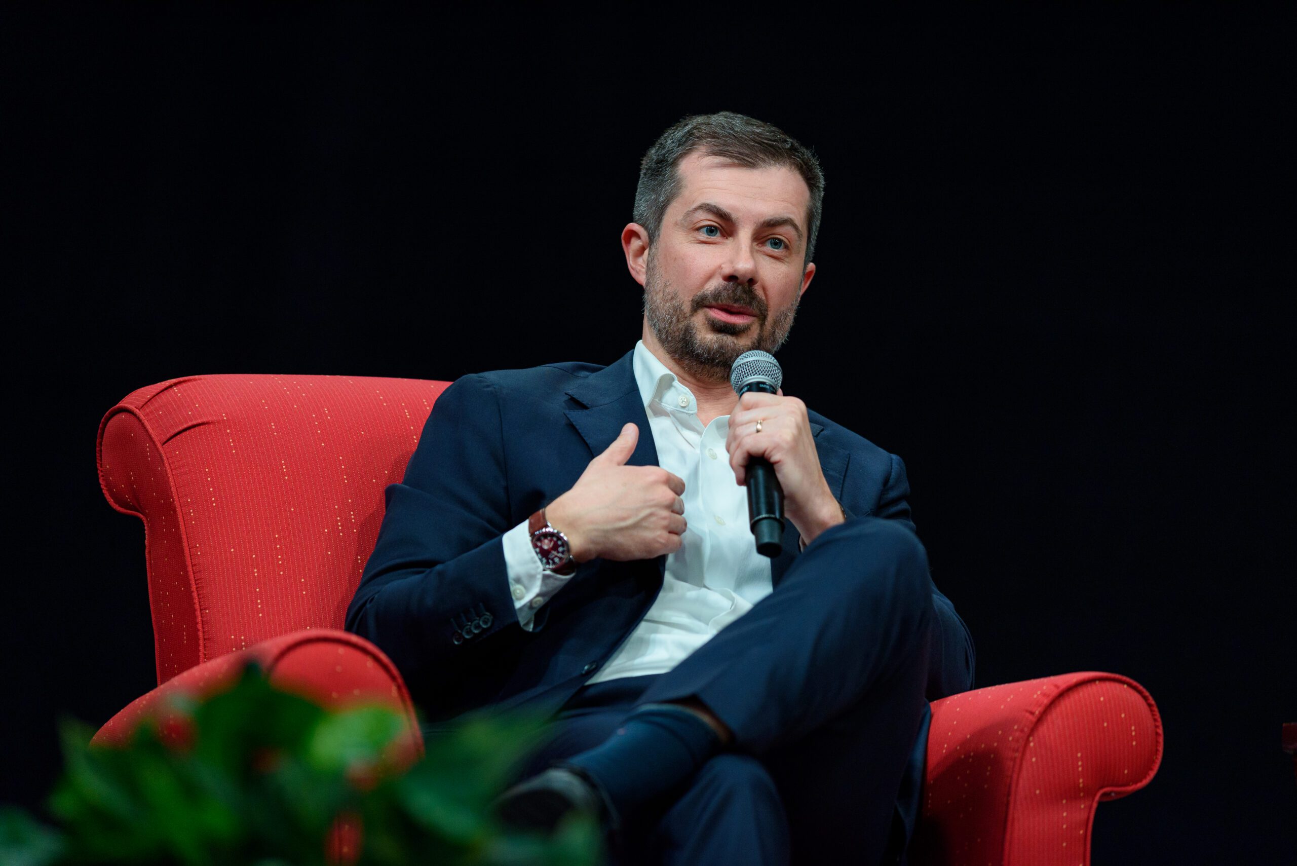 Pete Buttigieg sits in a red chair with a microphone in his hand