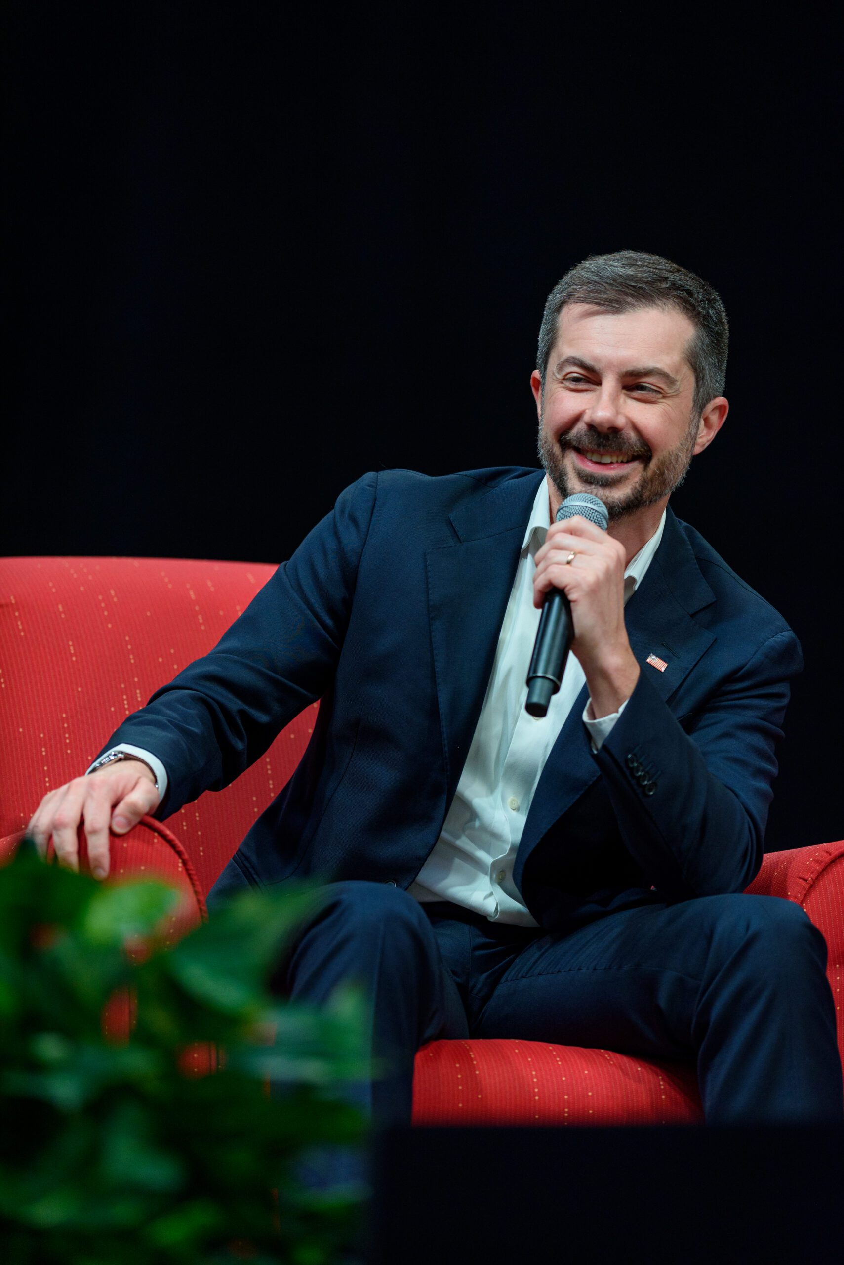 Pete Buttigieg sits in a red chair with a microphone in his hand