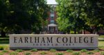 A stone marker with the words Earlham College with trees and a red brick building behind it