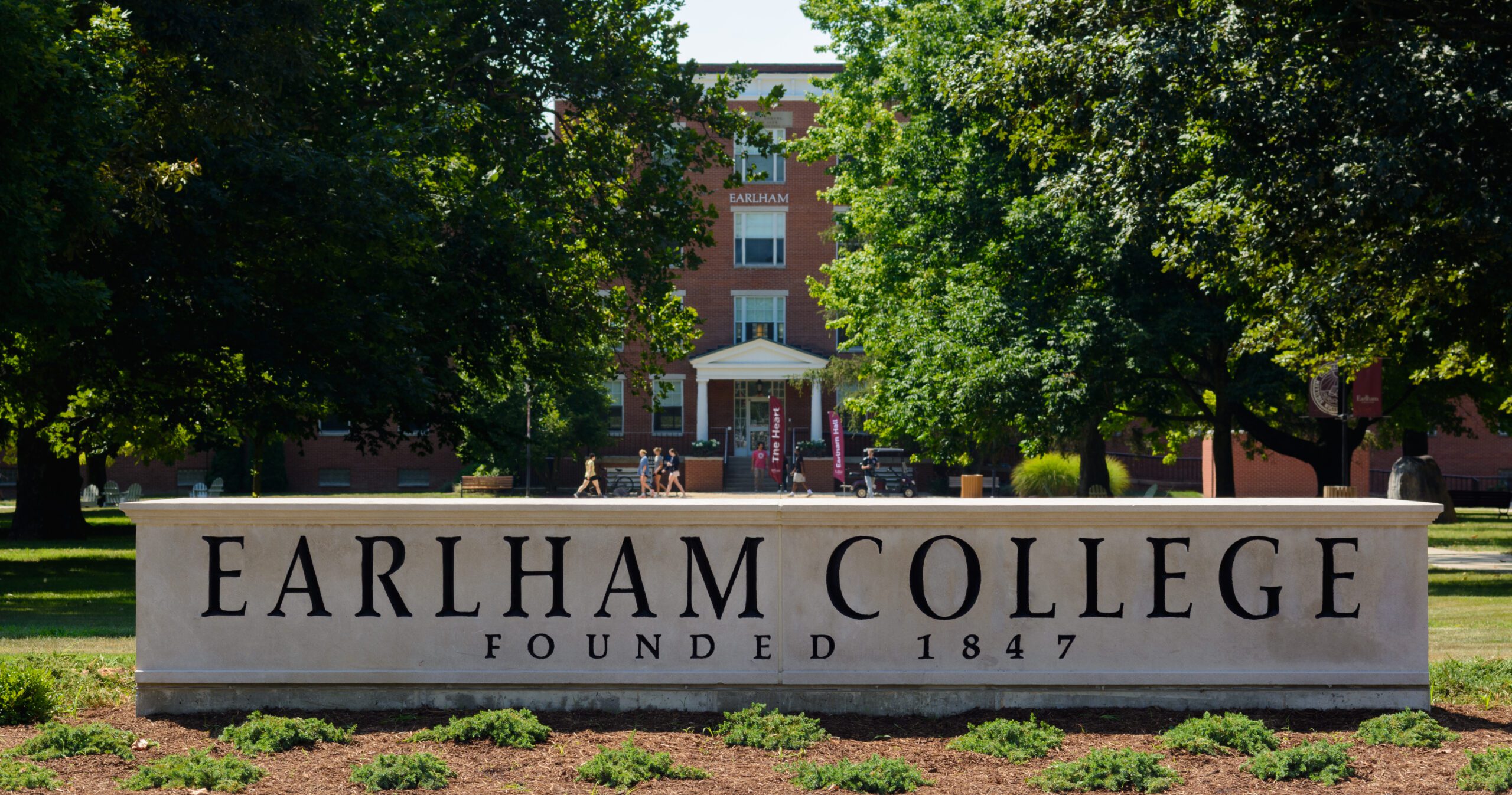 A stone marker with the words Earlham College with trees and a red brick building behind it