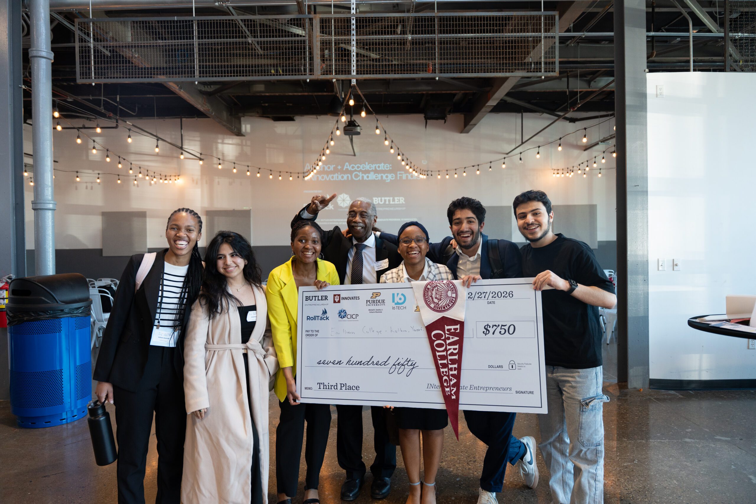 Six students and one faculty member from Earlham pose holding a giant check