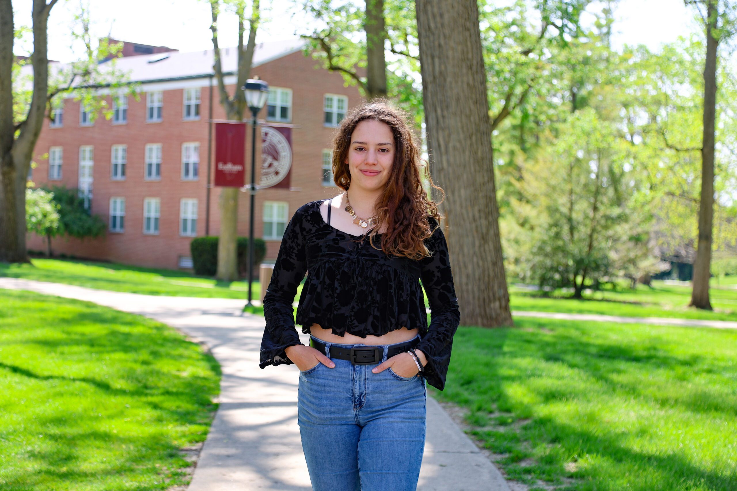 Briana Ancalmo stands on a paved sidewalk on the Earlham College campus with her hands in her pocket