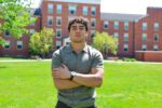 Armen Sargsyan stands in front of Earlham Hall wearing a gray polo shirt and with his arms crossed