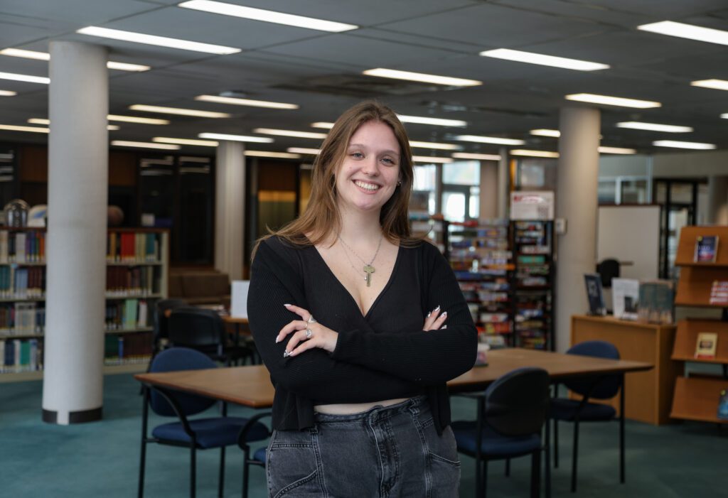 Reba McGloughlin stands in Lilly Library with her arms crossed with stacks of library books behind her