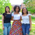 Three students pose in front of Earlham Hall on a sunny day