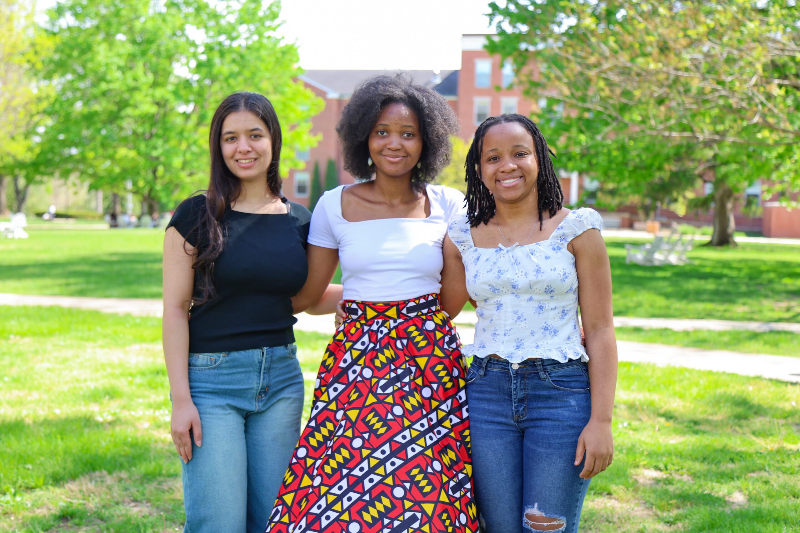 Three students pose in front of Earlham Hall on a sunny day