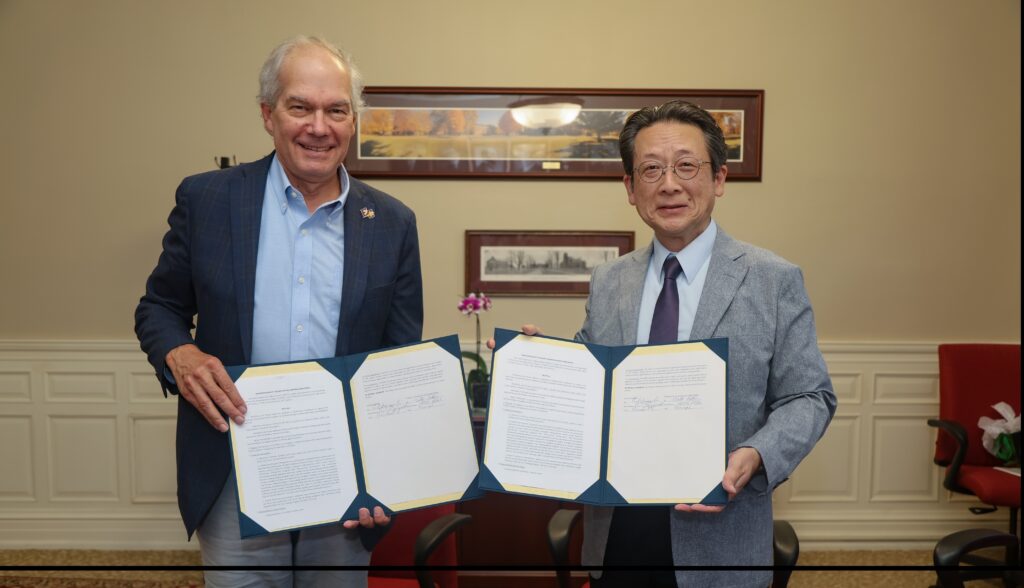 Earlham President Paul Sniegowski, standing left, and Friends School Tokyo Principal Naoto Aoki, standing right, hold signed agreements in portfolios in a meeting room on Earlham's campus.