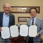 Earlham President Paul Sniegowski, standing left, and Friends School Tokyo Principal Naoto Aoki, standing right, hold signed agreements in portfolios in a meeting room on Earlham's campus.