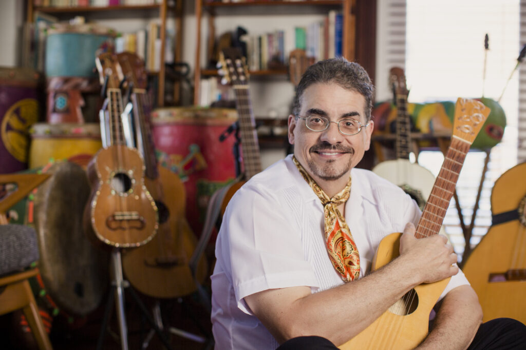 Juan Dies wraps his arms around an acoustic guitar while sitting in his Chicago apartment
