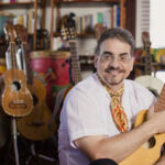 Juan Dies wraps his arms around an acoustic guitar while sitting in his Chicago apartment